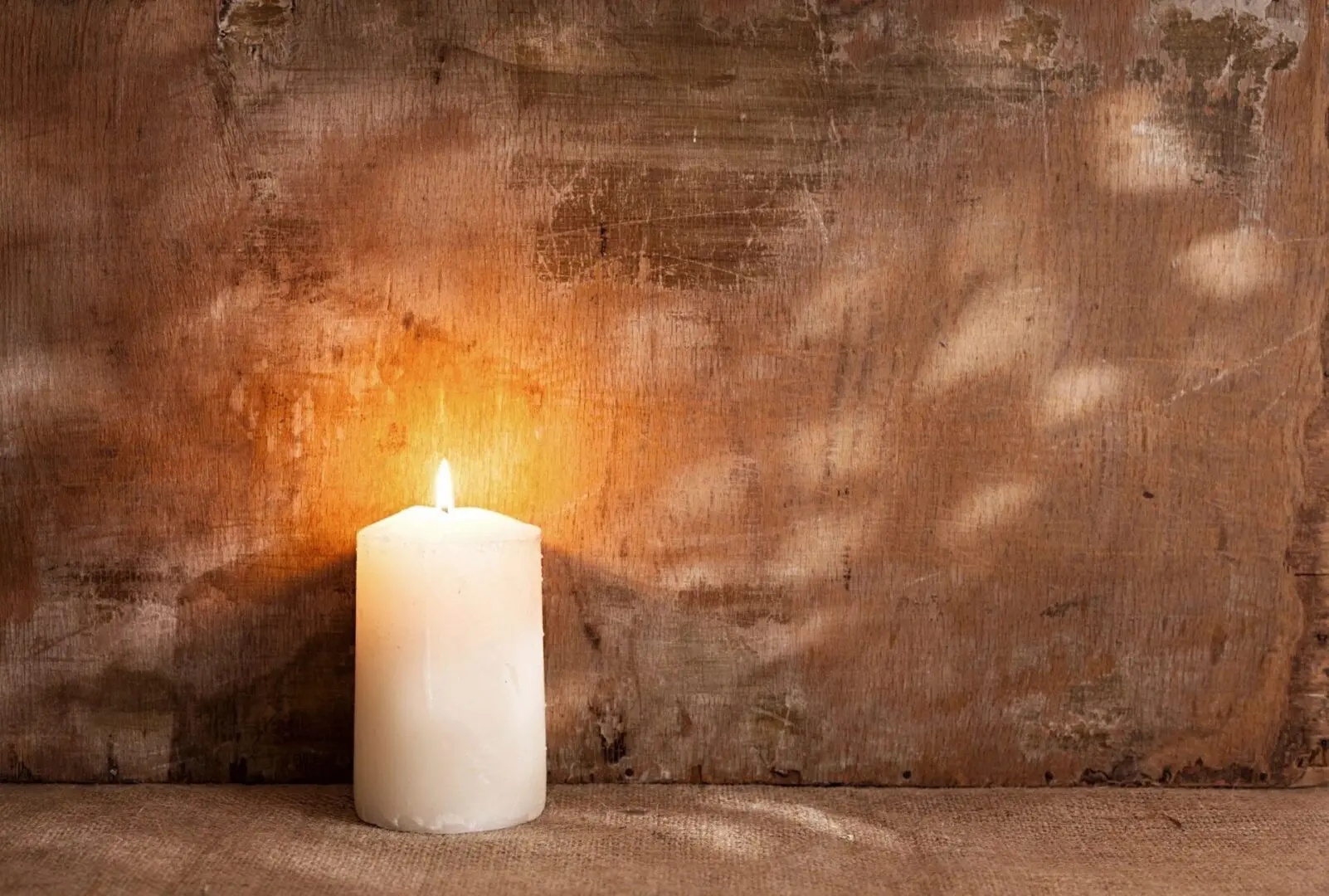 A candle lit in front of a brown wall.